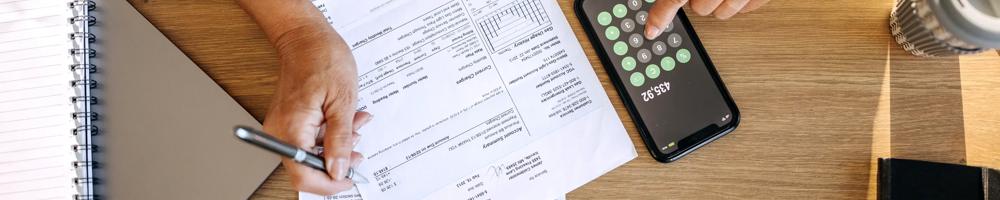 Unrecognisable person calculating expenses using mobile phone and paper documents