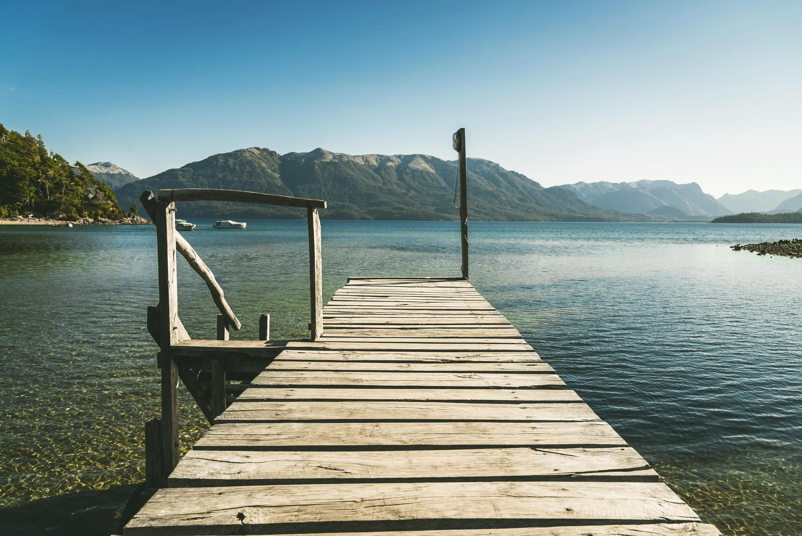 Landscape photo with old wooden pier, transparent lake water, and mountains. Concept of travel, lifestyle, harmony, summer, and vacations