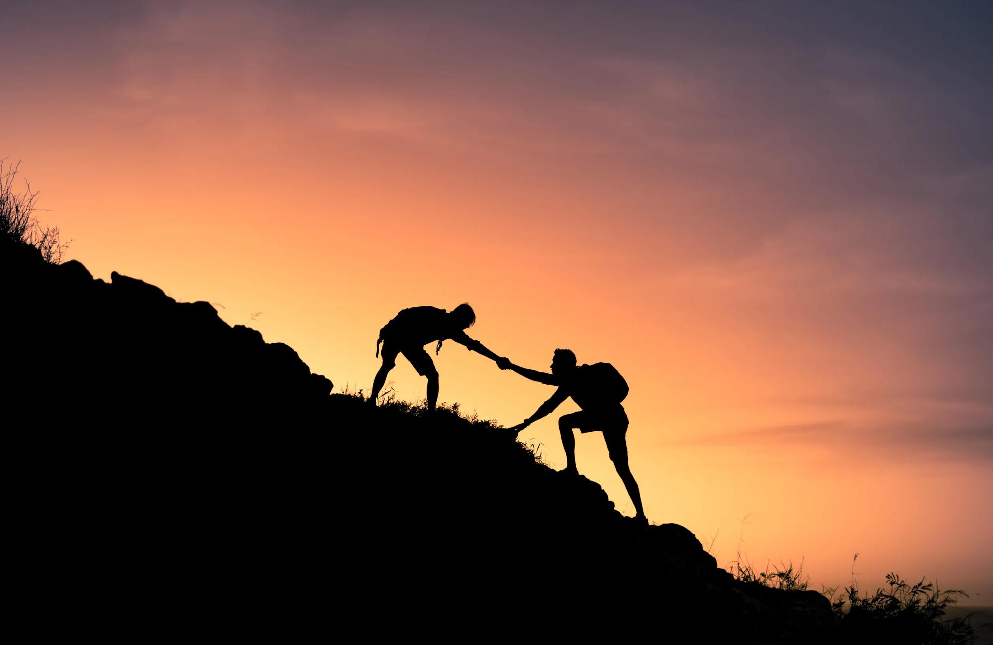 two people in silhouette climb a mountain at sunrise