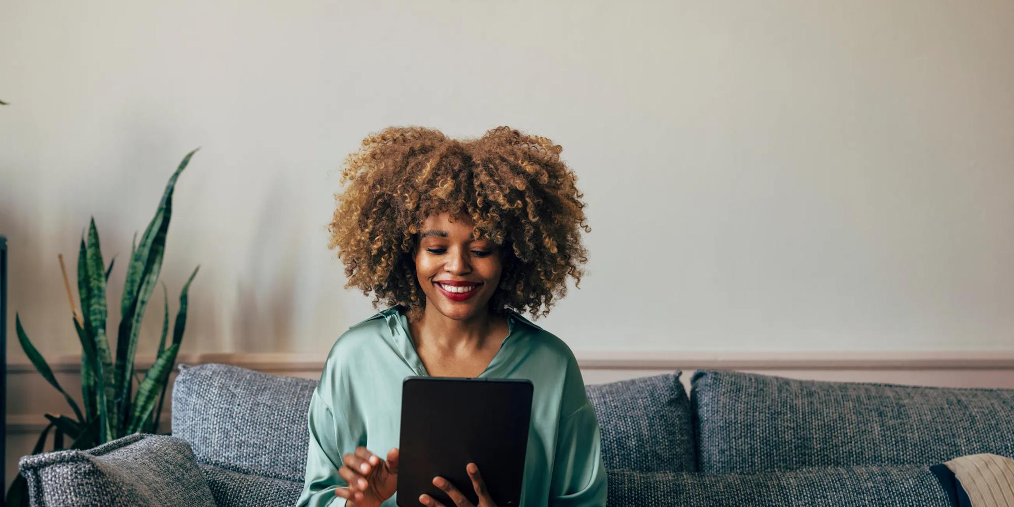 a woman happily uses her tablet on a couch