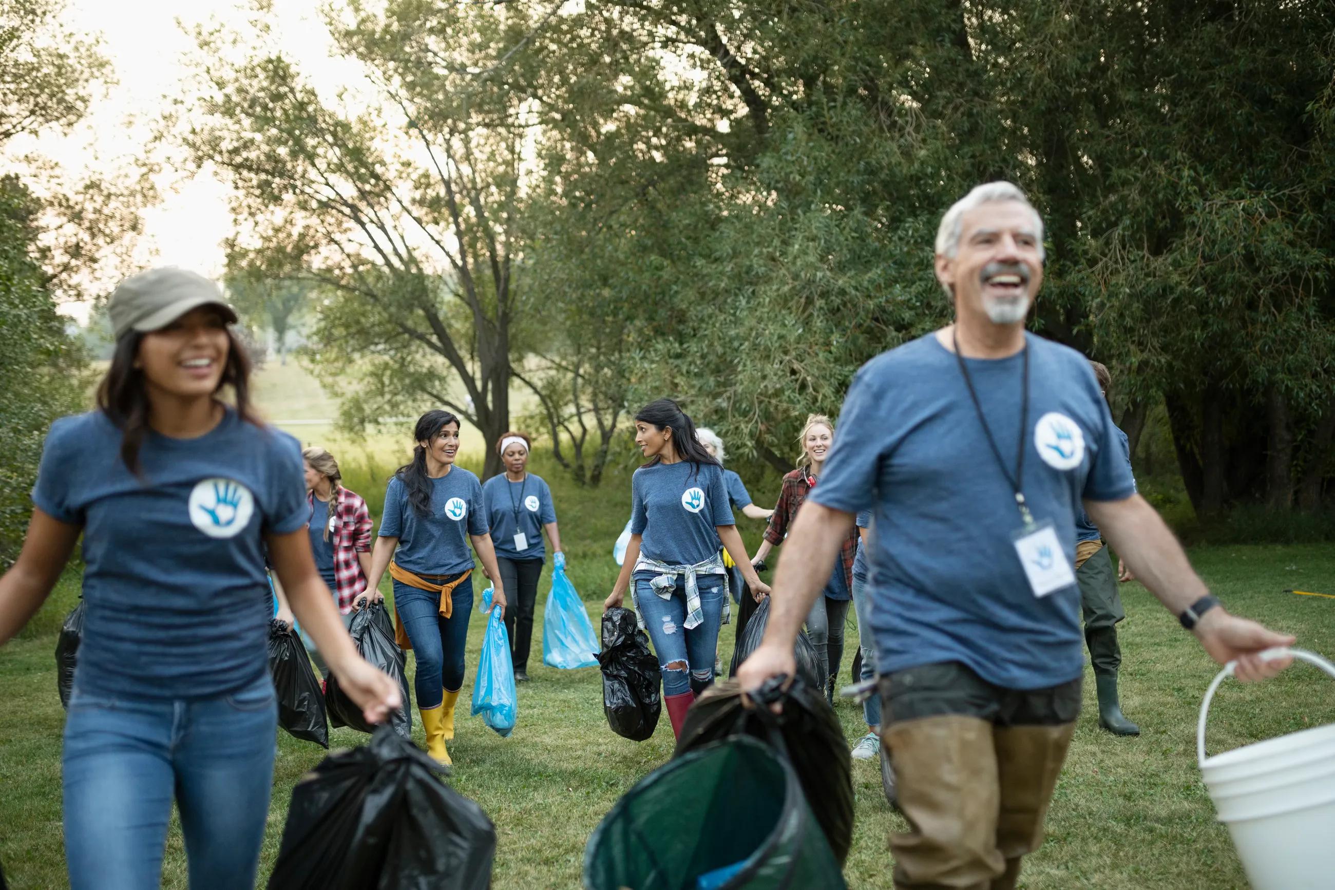 group of diverse, smiling adults carrying trash bags in a green space