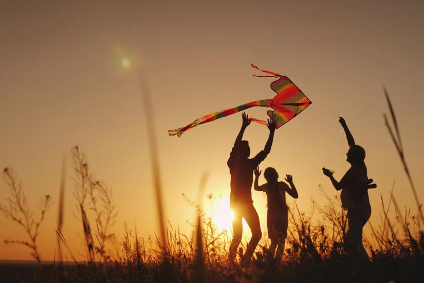 three people flying a kite at sunset